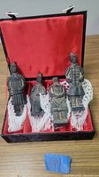 Four terra cotta style Chinese warrior statues in a black box with red lining, protected by white netting.