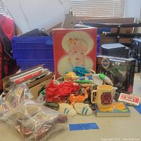 Wide view of assorted toys and collectibles including Barbie box, doll clothes, NASA and Exxon toys, mug, and other items on table.