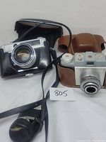 Front view of Kodak Pony 135 and Yashica Lynx 5000E cameras in cases with neck straps and vintage appearance.