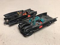 Photo showing the two vintage Husky Batmobile toy cars placed side by side revealing worn black paint and red Bat logos.