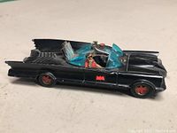 Side view of the black Vintage Corgi Batmobile featuring red bat logos on door and wheels, with visible wear.