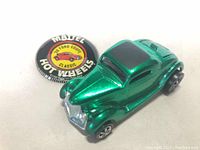 Metallic green Ford Coupe toy car and round Mattel Hot Wheels button badge displayed