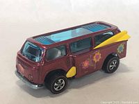 Front and left side view showing maroon bus body with blue transparent roof and yellow surfboard on side