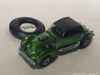 Front-left view of the metallic green Classic Cord with black roof and included promotional button badge behind.