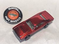 Circular Mattel Hot Wheels Custom Charger button badge alongside metallic red diecast Custom Charger car