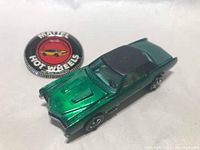 Top-down photo showing metallic green Hot Wheels Custom Eldorado redline car alongside the branded button badge