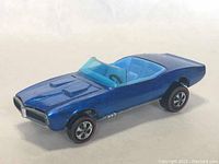 Front angle view showing blue paint, hood vents, front grille, translucent blue windshield, and five-spoke wheels with redline tires.