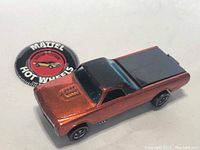 Close-up of vintage Mattel Hot Wheels Custom Fleetside redline toy truck in metallic orange with black roof and bed, with blue tinted windshield and detailed engine block on hood, showing wear.