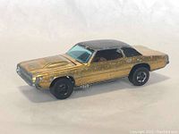 Front and side view of gold and black Custom T-Bird Hot Wheels car showing wear and paint chips on body and wheels.