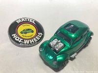 Close-up photo of the vintage green Hot Wheels Custom Volkswagen car alongside the round Mattel Hot Wheels button.