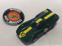 Photo showing green Hot Wheels Lola GT70 with yellow racing stripes numbered 10 and accompanying round badge.