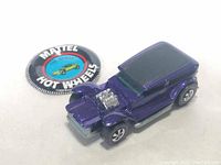 Top and side views of purple Hot Wheels The Demon car with chrome detailed engine and redline tires, displayed alongside a Mattel Hot Wheels circular button/badge.