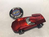 Top-down view of red metallic Hot Wheels Turbofire car with redline tires next to round promotional button with Hot Wheels logo and Turbofire car illustration.