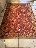 Full view of burgundy patterned area rug on tiled floor, showing overall design and proportions.