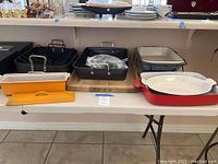 Full view of all cooking items including Calphalon roasting pans, cutting board, and Le Creuset casserole dishes