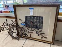 Framed print leaning against countertop alongside wreath and branch under natural light