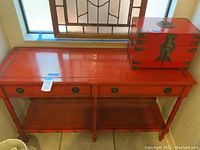 Full view of vintage red wooden foyer table with two drawers and cane shelf, and red Japanese jewelry box on top.