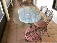 Overview of the outdoor dining table showing marble top under glass and four cushioned cast iron chairs on tiled porch floor.