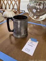 Vintage pewter beer pint mug placed on wooden table next to other household items.