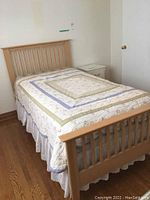 Full view of twin bed with wooden headboard and footboard, quilted bedding, and bed skirt in neutral bedroom environment.