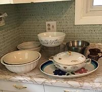 Full view of all bowls and serving pieces on countertop, showing white ceramic bowls, Pyrex bowl, stainless steel bowl, covered casserole, and other items