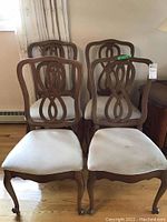Four dining room chairs arranged with wooden carved backs and upholstered seats showing wear and slight deformation.