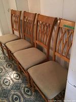 Six wooden dining chairs with beige upholstered seats aligned in a row on a patterned tile floor.