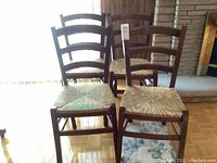 Front view of four wooden ladderback chairs with woven reed seats arranged in two rows with three visible floral cushions stacked under one chair.