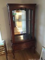 Full view of wooden china display cabinet with decorative glass door, two glass shelves inside, and drawer at bottom.