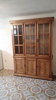 Front view of large wood and wood veneer china cabinet with glass doors in upper section and wooden doors in lower section.