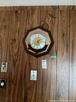 Octagonal wood framed battery-operated wall clock mounted on wood panel wall.