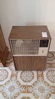 Front view of vintage Air King dehumidifier showing woodgrain exterior, vent, control dial, and power switch on tiled floor.