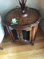 Full perspective of the round wooden end table showing front wire mesh door and scalloped edges on top.