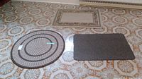 Photo showing two mats, a round rope mat approximately 3 feet diameter and a rectangular woven mat, both placed on patterned tile floor