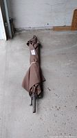 Closed brown patio umbrella laying on the ground, showing the fabric and the metal pole base without a stand.