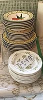 Stack of 6 matching bowls with yellow patterned rims and fruit designs, and 12 white bread and butter plates with green floral edging on table