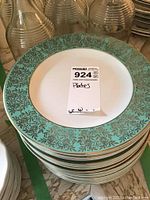 Stack of dinner plates with white center and turquoise floral gold patterned rim.