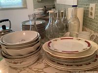 Wide view of porcelain bowls stacked with glass bottles and various platters nearby.