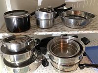 Photo showing stacked stainless steel pots, saucepans, lids, and a metal colander.