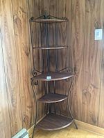 Full view of the corner shelving unit showing metal frame, wood shelves, and overall condition against wood-paneled wall.