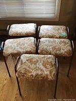 Five stools arranged close together showing tops with brown and tan leaf patterned vinyl upholstery and metal frames.