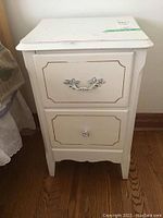 Front view of white bedside table showing two drawers with decorative molding and metal handles