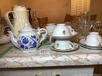 Image shows a white teapot with blue flower design and 3 white cups with matching saucers upside down.
