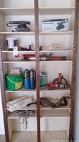 Shelf containing Black & Decker finishing sander, Stanley wood plane, Milwaukee drill, Mastercraft mitre box, slug and snail killer bottle, caulking tools, clamps, and propane torch cylinders.