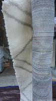 Photo showing the white shag area rug with gray lines next to the tightly rolled multicolored striped rug.