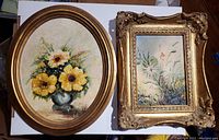 Two vintage framed oil paintings side by side; one oval floral bouquet painting, one rectangular natural landscape with ornate gold frame