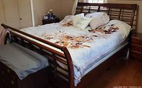 Photo showing king size wooden bed frame with floral bedding set. Medium-tone wood frame with slatted headboard and footboard visible. Wear and scratches on wood can be seen.