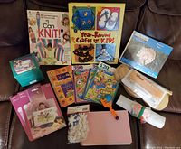 Overview photo of assorted kids craft kits, knitting books, magic trick props packaged and rolled, sticker books, and small crafting tools on a brown couch.