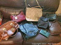 Overview of seven assorted purses and one wallet arranged on a brown leather couch, showing varied styles and colors including red, tan, black, brown, and green.