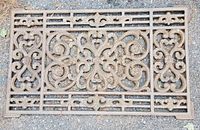 Top-down image of vintage heavy duty cast iron door mat showing detailed ornamental floral and scrollwork design.
